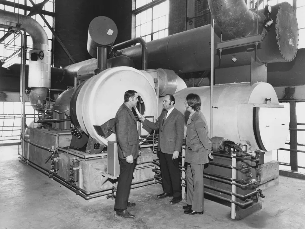 Black and white photo of three men talking in front of machinery
