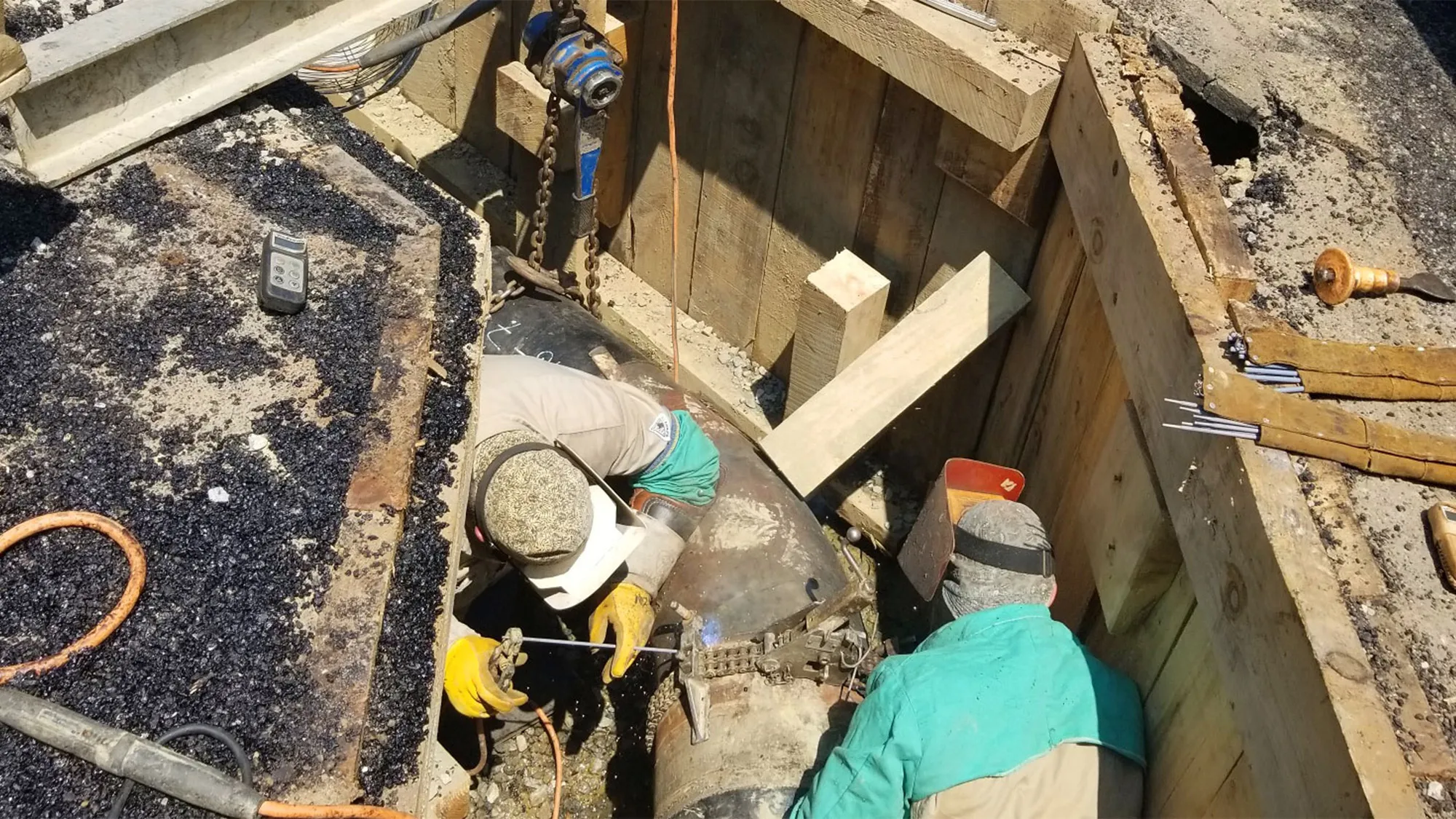 Two workers welding a pipe in a trench
