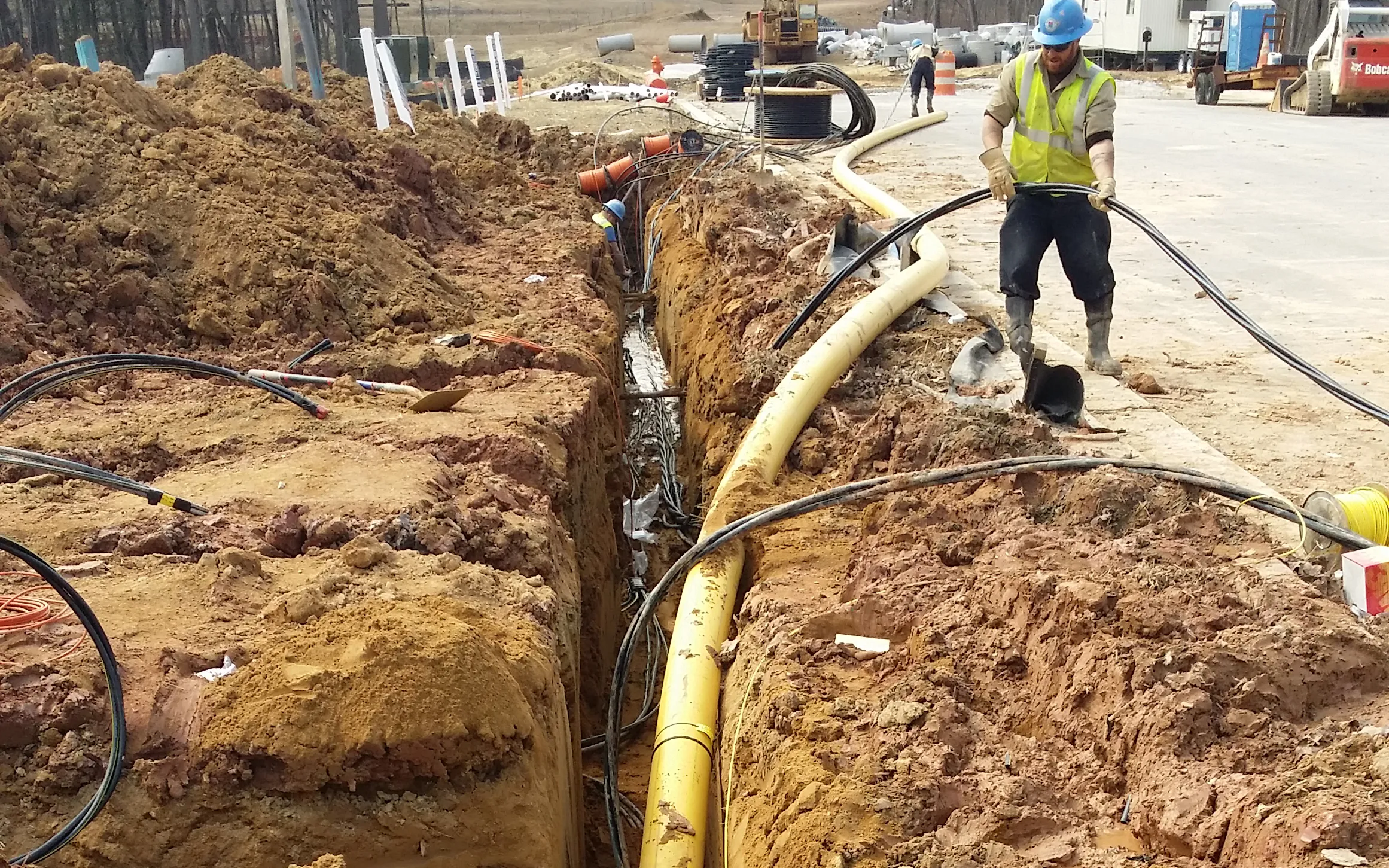 Worker putting electrical piping into trench