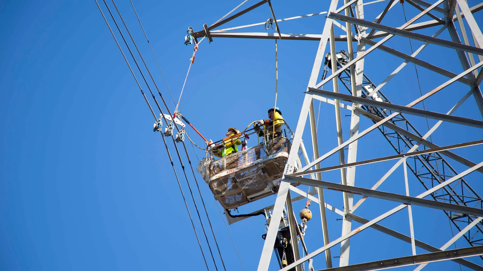 Workers in a bucket from a bucket truck working on transmission lines